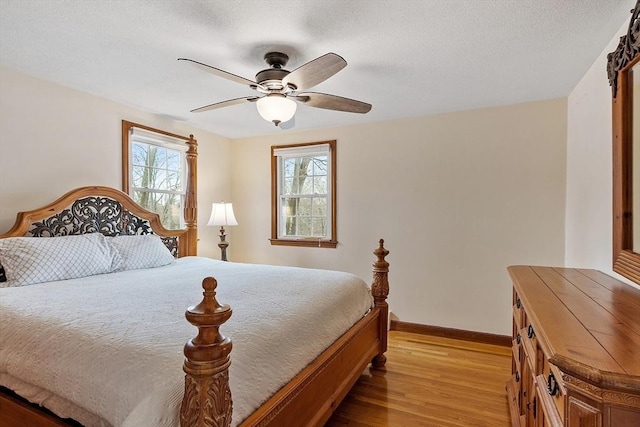 bedroom featuring light wood-style flooring, a textured ceiling, baseboards, and a ceiling fan