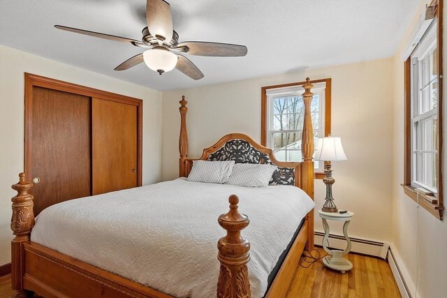 bedroom featuring a ceiling fan, light wood-style floors, a closet, and a baseboard radiator