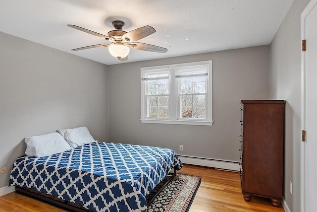 bedroom featuring a baseboard heating unit, light wood-style flooring, a ceiling fan, and baseboards