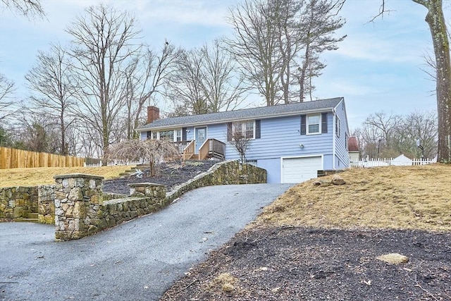 view of front facade with aphalt driveway, a chimney, an attached garage, and fence