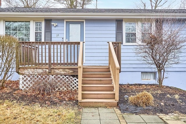 entrance to property featuring a deck and roof with shingles