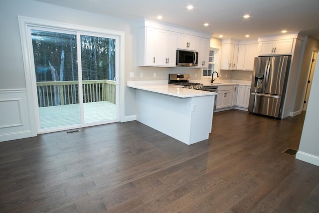 kitchen with light countertops, appliances with stainless steel finishes, a peninsula, white cabinets, and dark wood-type flooring