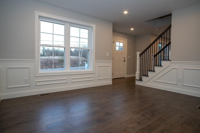 foyer entrance with stairs, visible vents, a decorative wall, and dark wood-style flooring