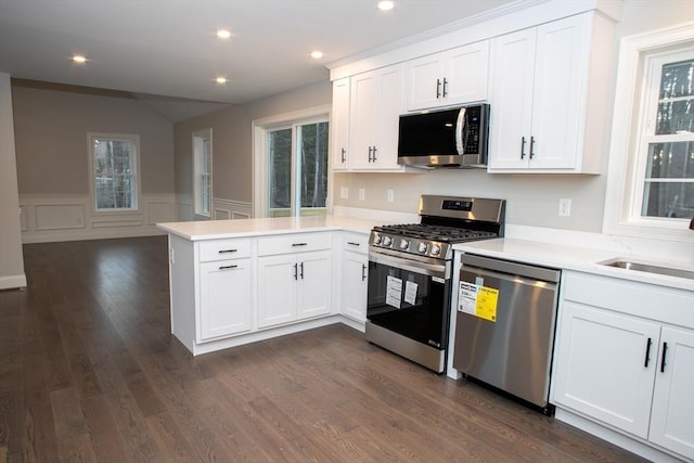 kitchen with light countertops, stainless steel appliances, a wainscoted wall, white cabinets, and a peninsula