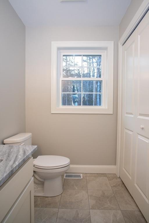 half bath featuring toilet, vanity, baseboards, and visible vents