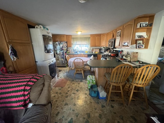 kitchen with a breakfast bar area, kitchen peninsula, stacked washer and clothes dryer, and appliances with stainless steel finishes