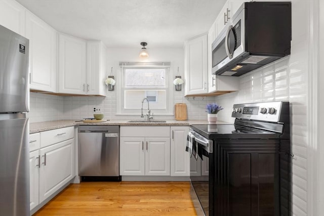 kitchen featuring appliances with stainless steel finishes, a sink, decorative backsplash, white cabinets, and light wood-style floors