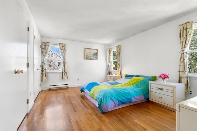 bedroom featuring light wood-type flooring, a baseboard heating unit, and baseboards