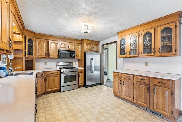 kitchen featuring stainless steel appliances, glass insert cabinets, brown cabinetry, light countertops, and light floors