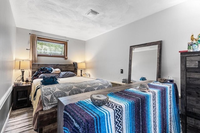 bedroom with a textured ceiling, visible vents, and wood finished floors