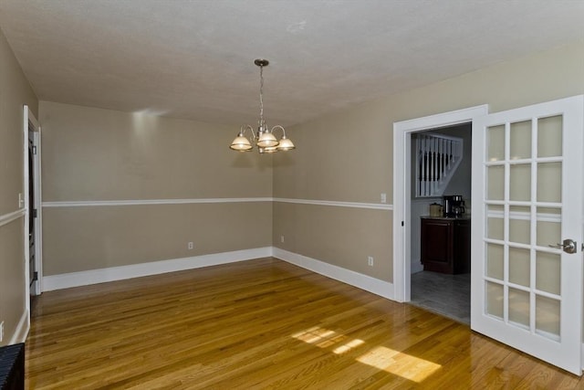 unfurnished dining area with a notable chandelier, baseboards, and wood finished floors