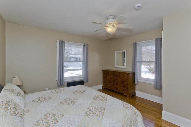 bedroom featuring a ceiling fan, radiator heating unit, baseboards, and wood finished floors