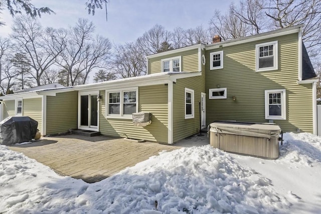 snow covered back of property featuring a hot tub, a chimney, and a patio