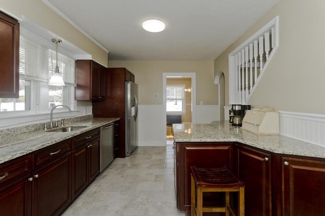 kitchen with stainless steel appliances, dark brown cabinets, wainscoting, and a sink