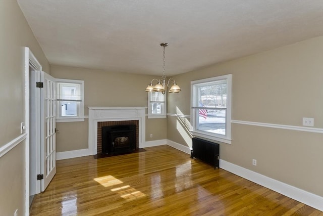 unfurnished living room with radiator heating unit, an inviting chandelier, wood finished floors, and baseboards