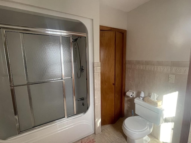 bathroom featuring toilet, shower / bath combination with glass door, tile patterned flooring, and tile walls