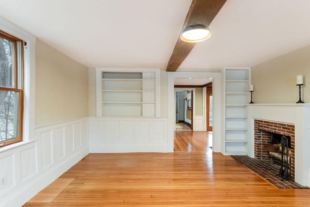 unfurnished living room with built in shelves, a healthy amount of sunlight, and light hardwood / wood-style floors