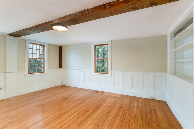 spare room featuring light wood-type flooring, a wealth of natural light, built in features, and beam ceiling