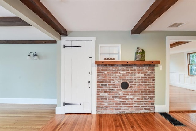 unfurnished living room featuring beamed ceiling and light wood-type flooring