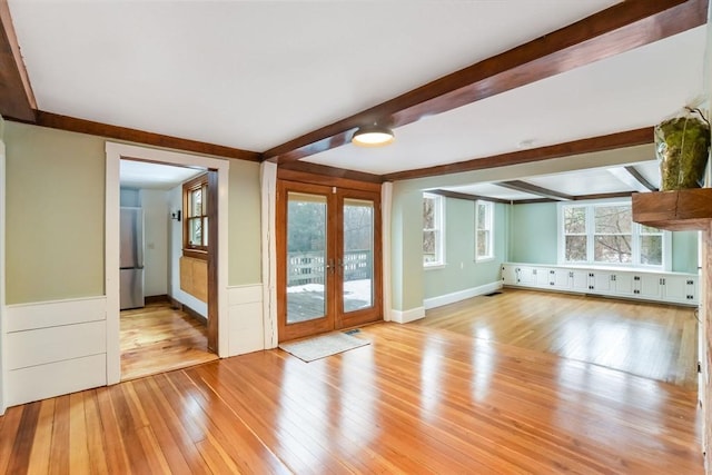 unfurnished living room featuring light wood-type flooring, beam ceiling, and french doors