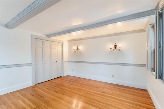 unfurnished room with ornamental molding, light wood-type flooring, and beam ceiling