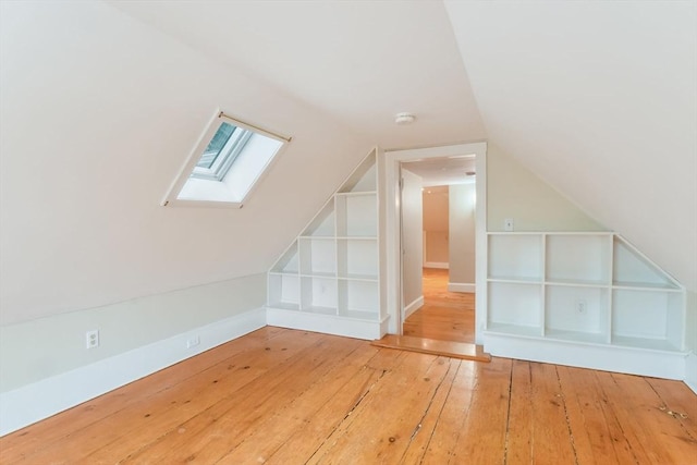 additional living space with built in shelves, vaulted ceiling with skylight, and hardwood / wood-style floors