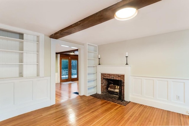 unfurnished living room with beamed ceiling, built in features, light hardwood / wood-style floors, and french doors