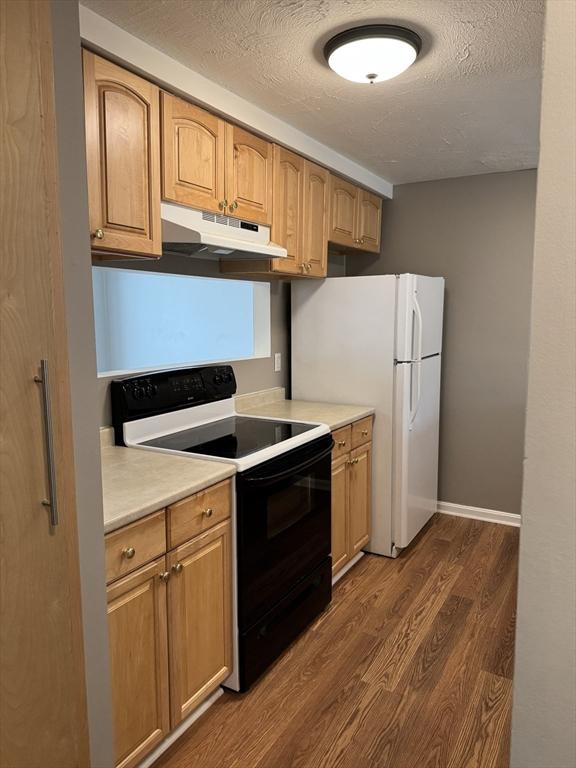 kitchen with dark wood-type flooring, range with electric cooktop, under cabinet range hood, a textured ceiling, and light countertops