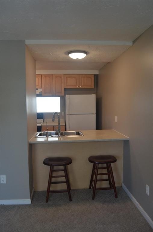 kitchen with a breakfast bar, a peninsula, freestanding refrigerator, light brown cabinetry, and a sink