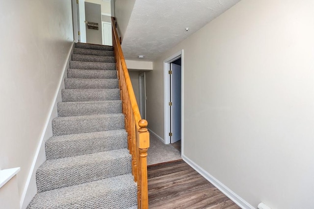 staircase featuring wood finished floors, baseboards, and a textured ceiling