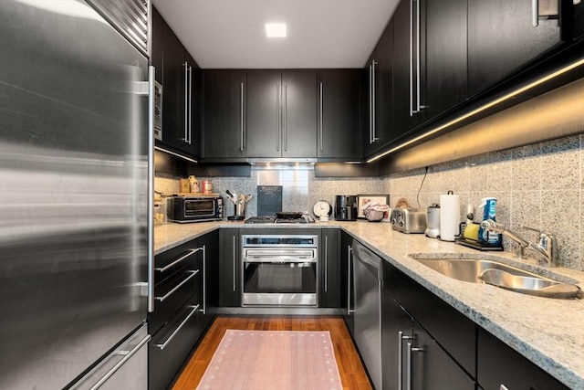 kitchen featuring tasteful backsplash, a sink, dark wood-style flooring, dark cabinetry, and stainless steel appliances