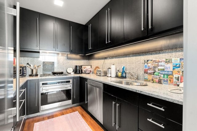kitchen with tasteful backsplash, dark cabinetry, stainless steel appliances, light wood finished floors, and a sink