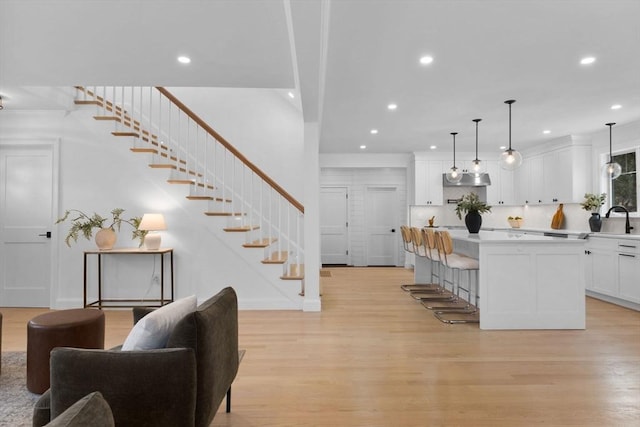 kitchen with light wood finished floors, a sink, a center island, white cabinets, and light countertops