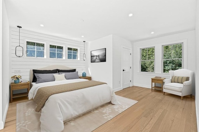 bedroom with recessed lighting, light wood-type flooring, baseboards, and wooden walls