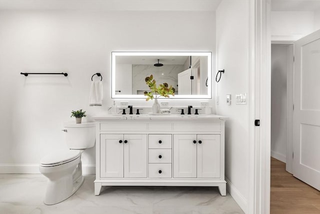 full bath with baseboards, toilet, double vanity, marble finish floor, and a sink