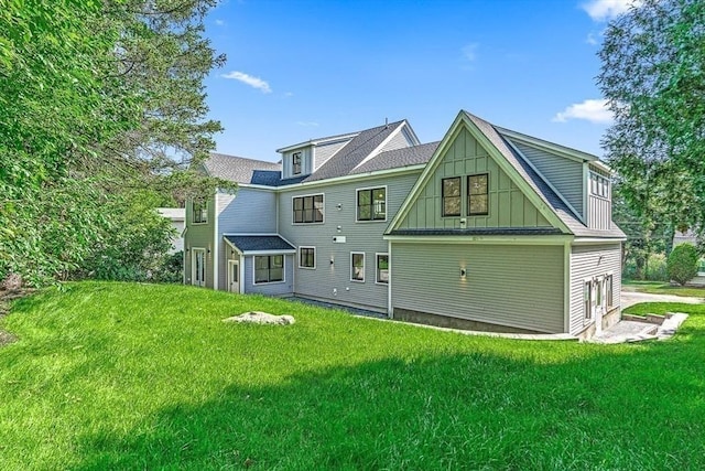 rear view of house featuring board and batten siding, a yard, and roof with shingles