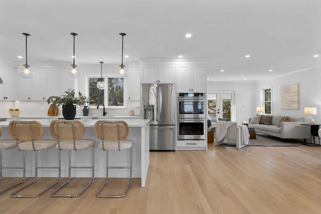 kitchen featuring white cabinetry, stainless steel appliances, light countertops, a kitchen bar, and light wood-type flooring