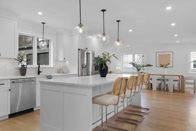 kitchen featuring light wood-style flooring, light countertops, appliances with stainless steel finishes, a kitchen breakfast bar, and tasteful backsplash