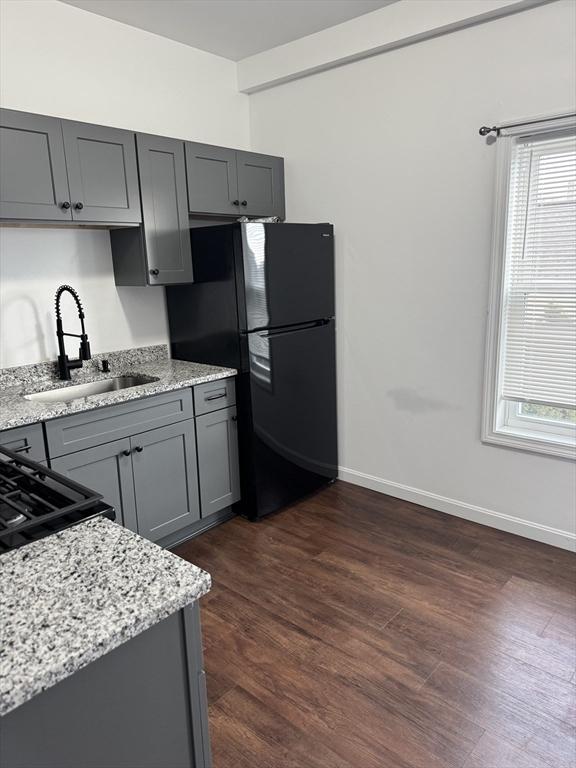 kitchen featuring black refrigerator, light stone counters, a healthy amount of sunlight, sink, and gray cabinets