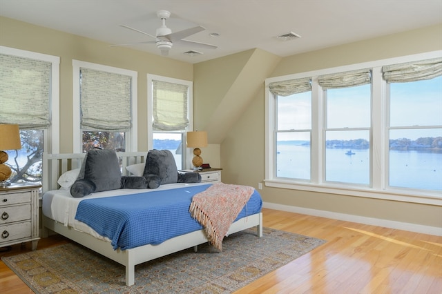 bedroom featuring multiple windows, hardwood / wood-style floors, a water view, and ceiling fan