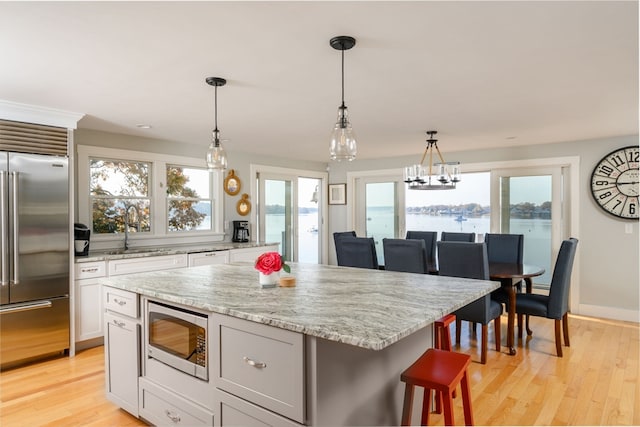 kitchen with built in appliances, pendant lighting, light hardwood / wood-style floors, a center island, and a water view