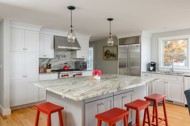 kitchen featuring appliances with stainless steel finishes, light wood-type flooring, wall chimney range hood, and a kitchen island