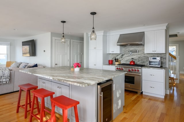 kitchen with wall chimney range hood, a kitchen bar, a center island, beverage cooler, and premium stove