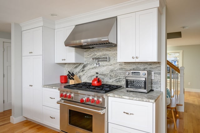 kitchen with light wood-type flooring, wall chimney exhaust hood, premium stove, and white cabinets