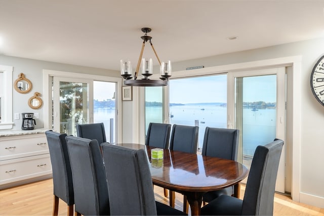 dining space with an inviting chandelier, a water view, and light wood-type flooring