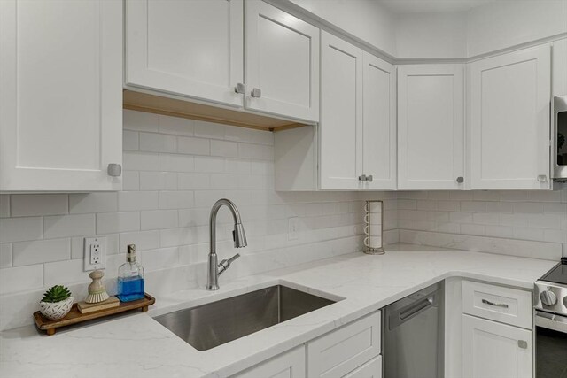 kitchen featuring white cabinets, light stone countertops, appliances with stainless steel finishes, a sink, and backsplash