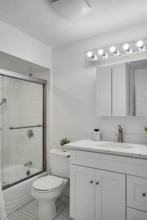 full bathroom featuring vanity, toilet, a textured ceiling, tile patterned floors, and enclosed tub / shower combo