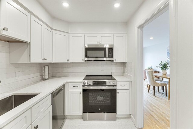 kitchen with stainless steel appliances, light stone counters, white cabinetry, and a sink