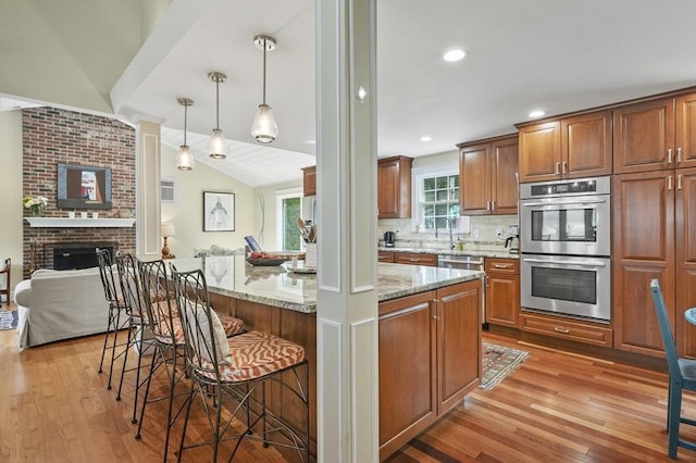 6 Lous Dr, Dudley, MA 01571 - kitchen featuring stainless steel appliances, light wood-style floors, a breakfast bar area, light stone counters, and brown cabinets