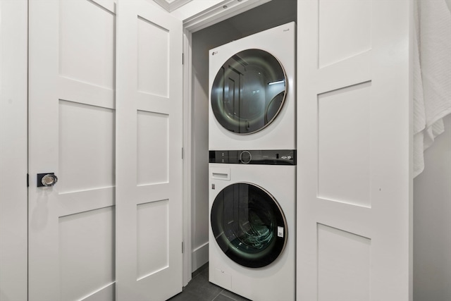 laundry area with dark tile patterned floors and stacked washer / drying machine